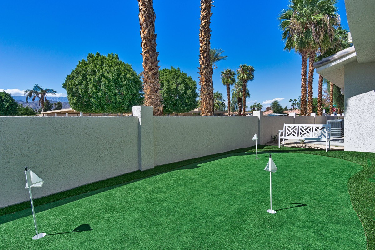 A well-maintained outdoor putting green surrounded by palm trees and a white fence.