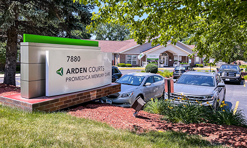 A sign for Arden Courts with a building and parked cars in the background.