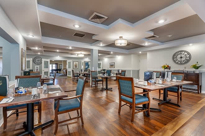 A modern dining room with neatly arranged tables and chairs, featuring wooden floors and elegant lighting.