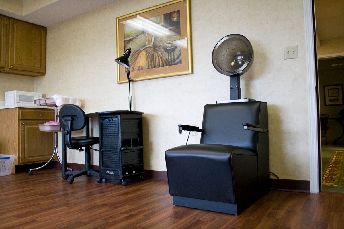 A salon interior featuring a hair dryer chair and a workspace desk beside a painting.