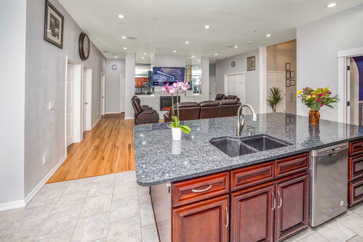 Modern open floor plan kitchen and living area with granite countertops and wood flooring.