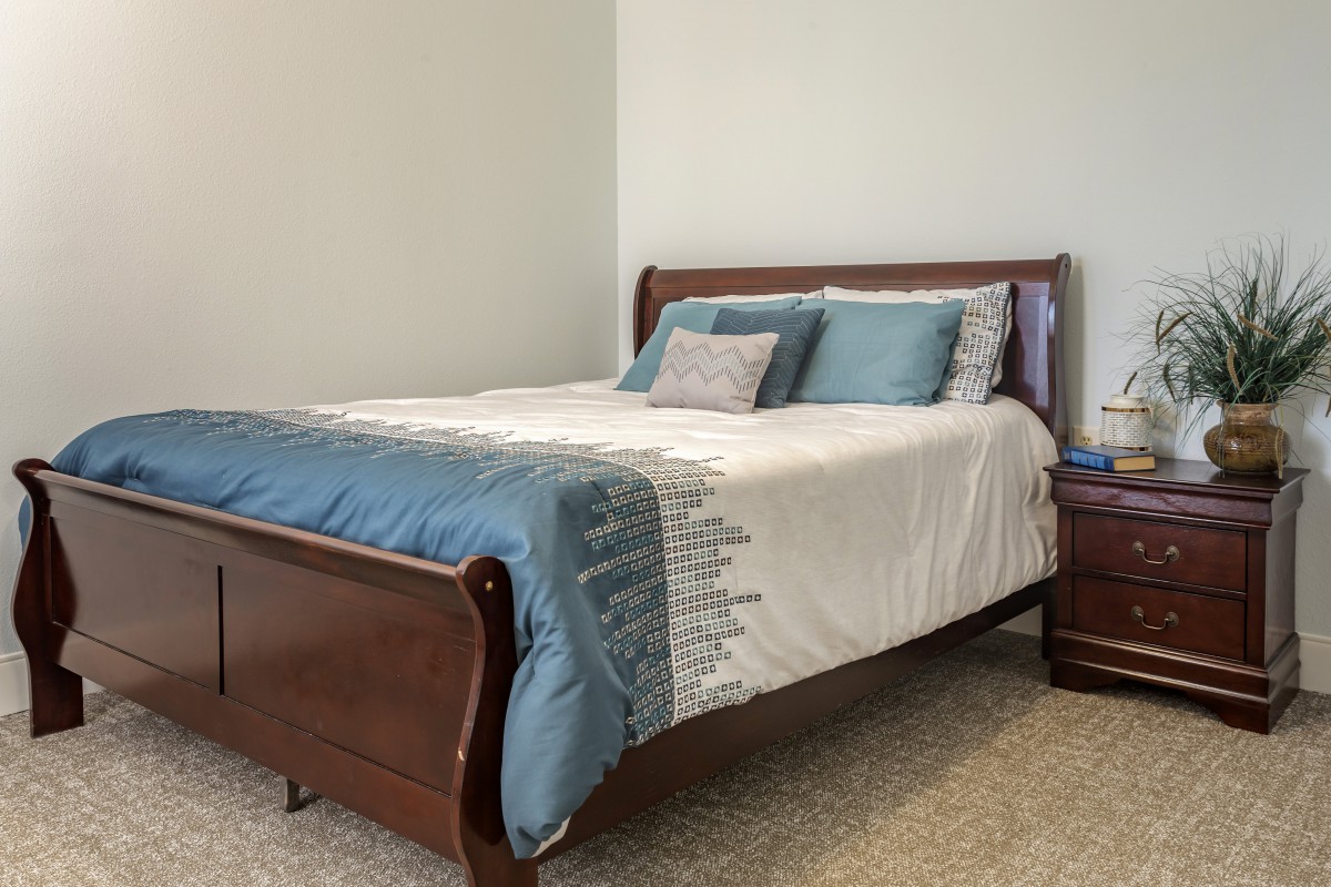 A neatly arranged bedroom with a wooden bed frame, adorned with white and blue bedding and pillows.