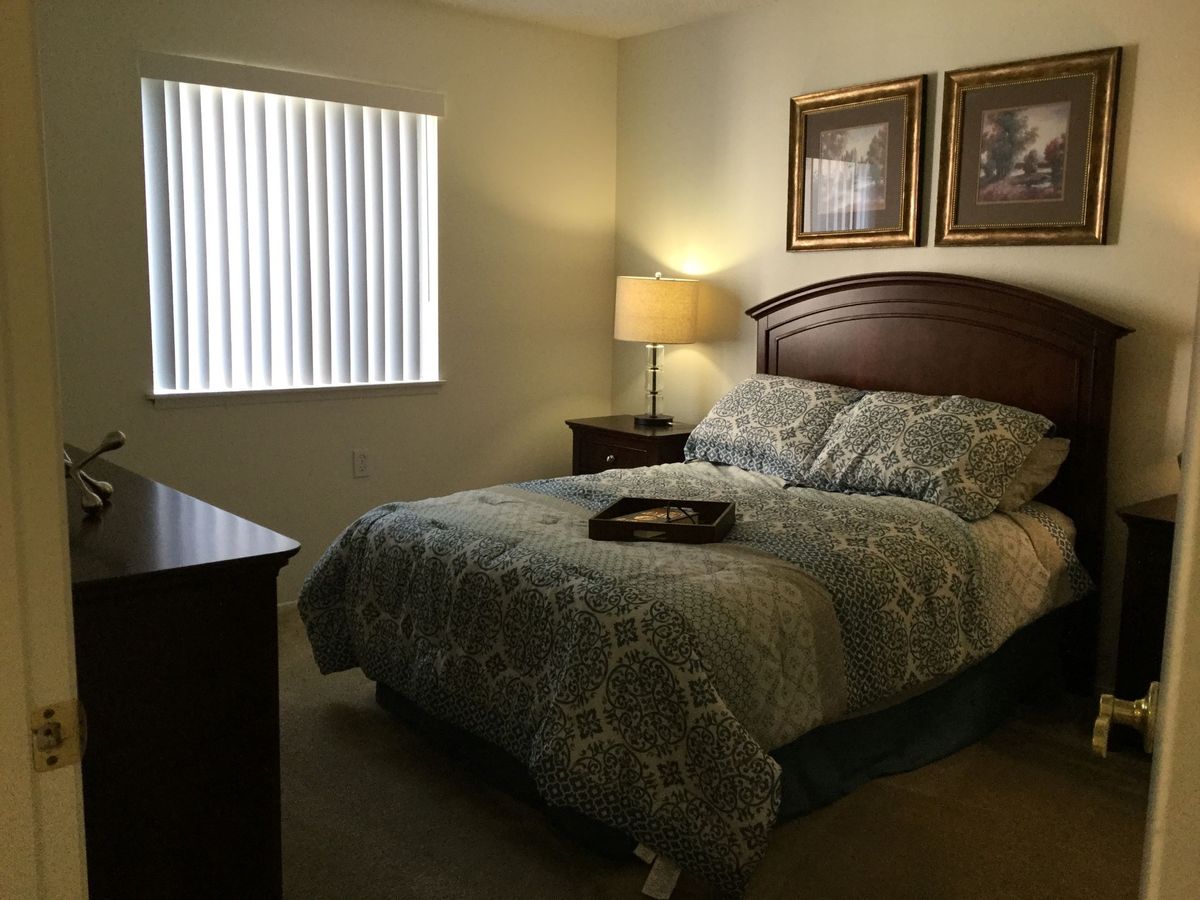 A cozy bedroom with a neatly made bed, a bedside lamp, and framed artwork on the walls.