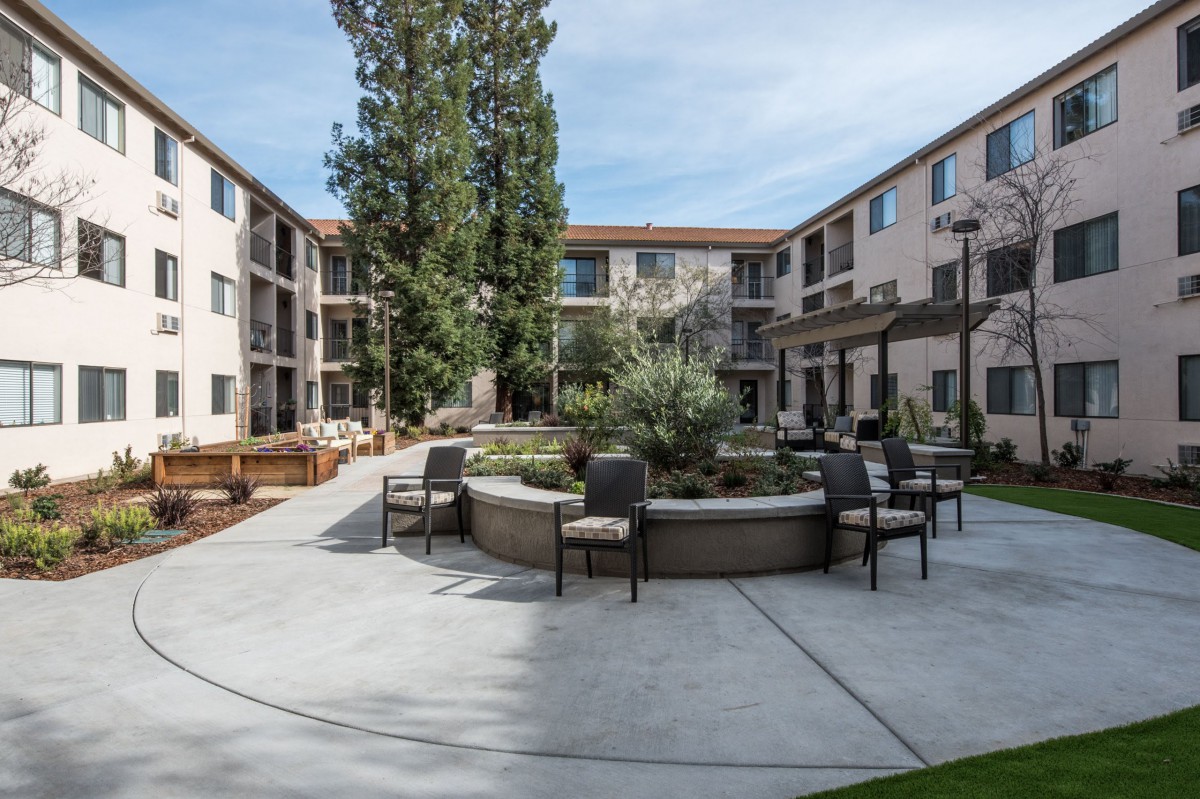 A peaceful courtyard with seating surrounded by a multi-story apartment building.