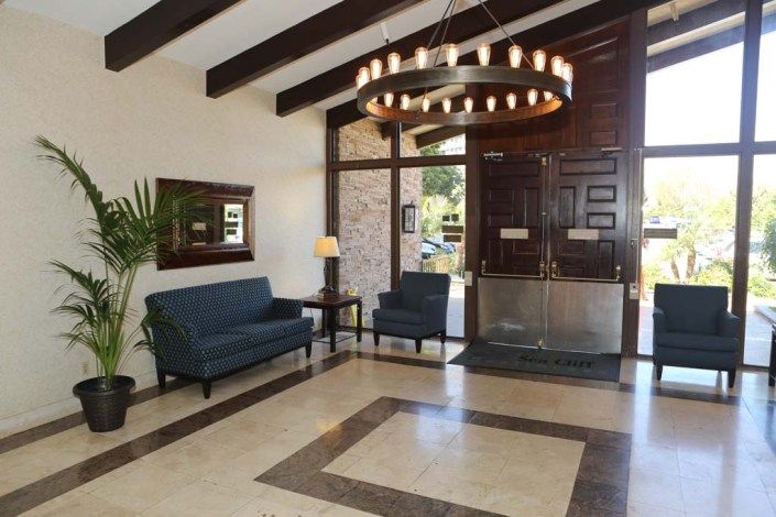 A spacious lobby area with blue sofas and a chandelier, featuring wooden ceiling beams and a large entrance.