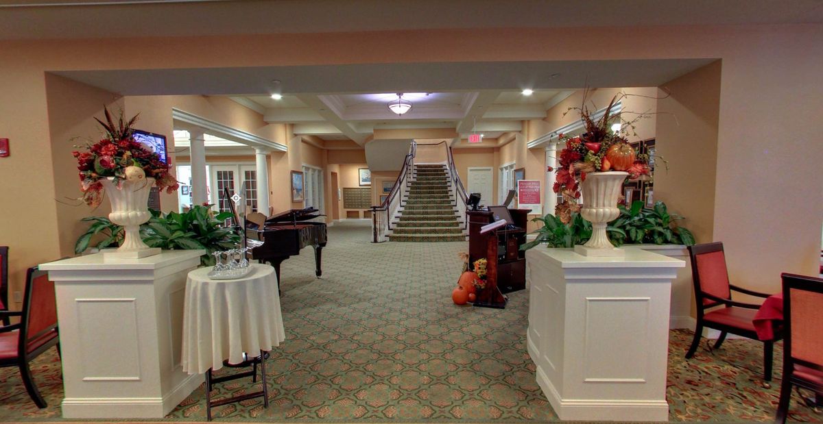A spacious lobby area featuring a grand piano, decorative plants, and an elegant staircase.