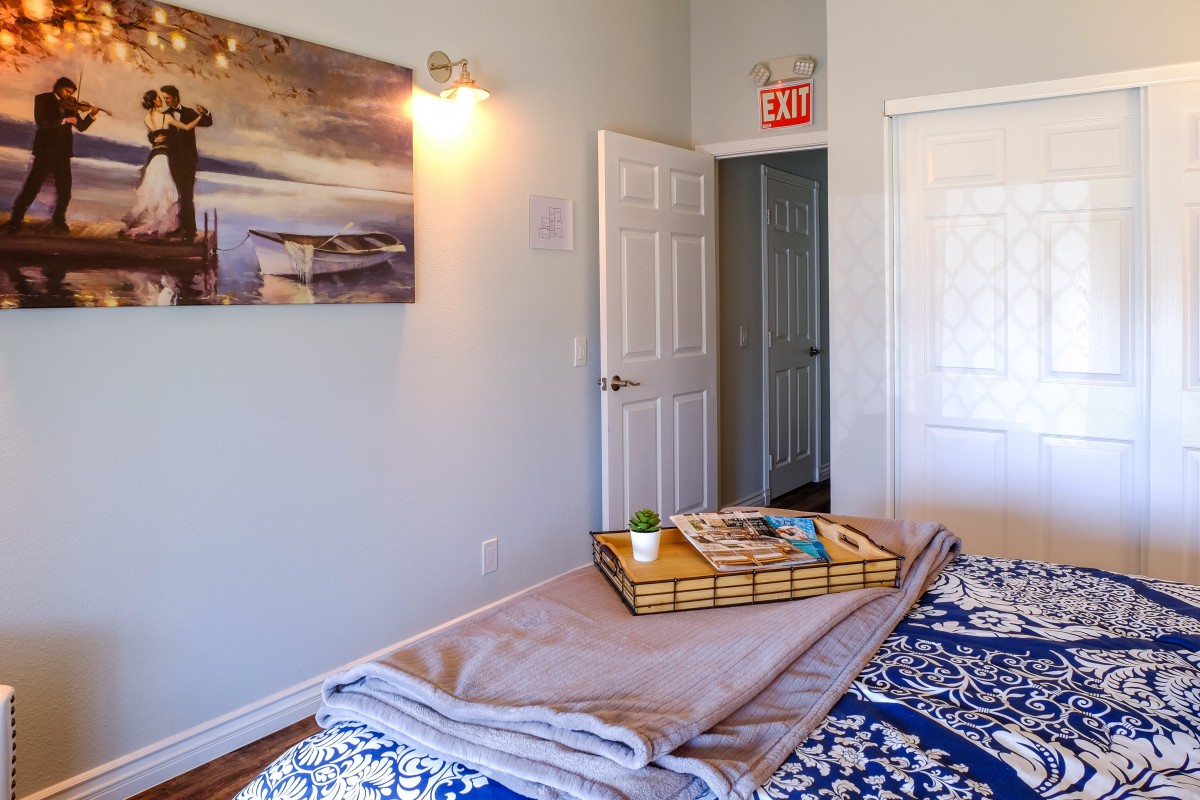 A cozy bedroom with a neatly arranged bed featuring a decorative tray, artwork on the wall, and an open door leading to another room.