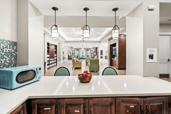 A modern kitchen with white countertops and wood cabinetry, featuring pendant lighting and an open layout.