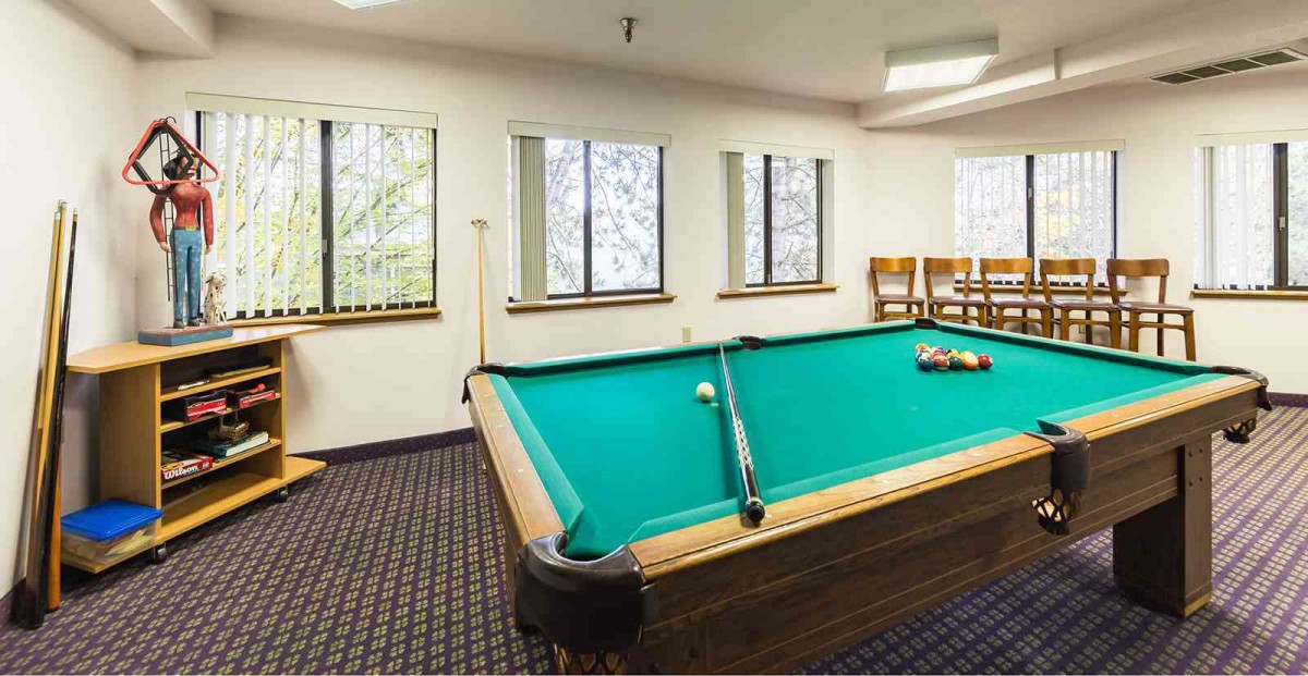 A cozy billiards room with a pool table and seating area by the windows.