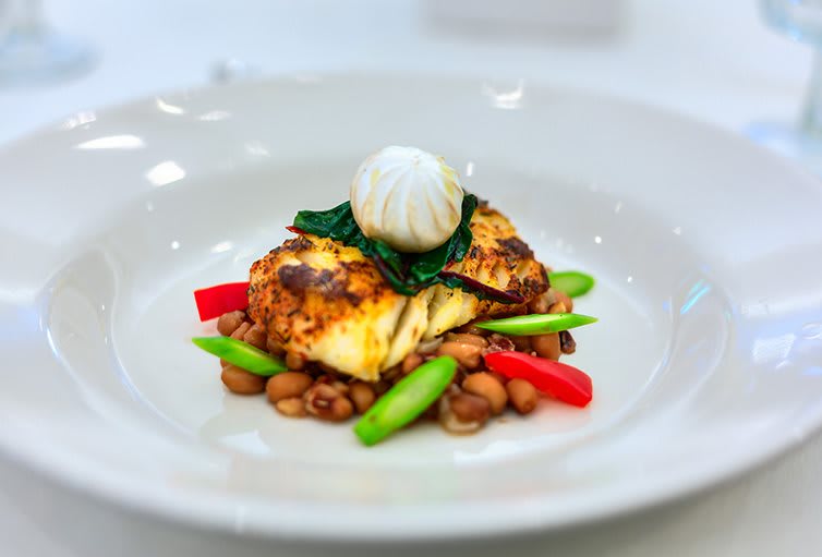 A gourmet fish dish served with asparagus, beans, and a garlic garnish.