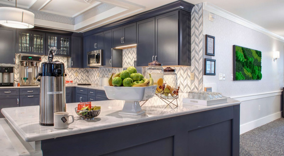 A modern kitchen with dark cabinets, a chevron backsplash, and a fruit display on the island.