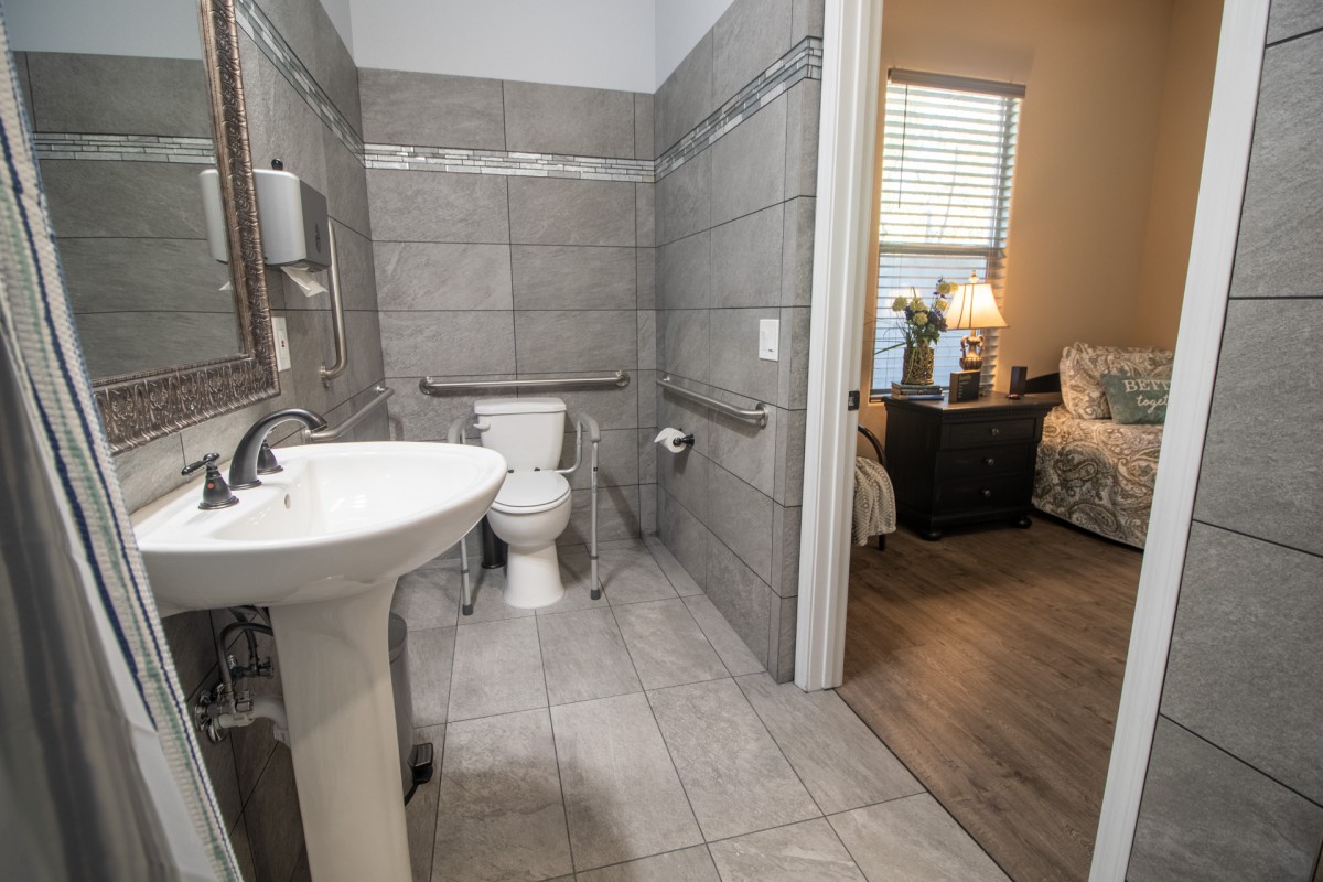 A modern bathroom with tiled walls connected to a cozy bedroom.