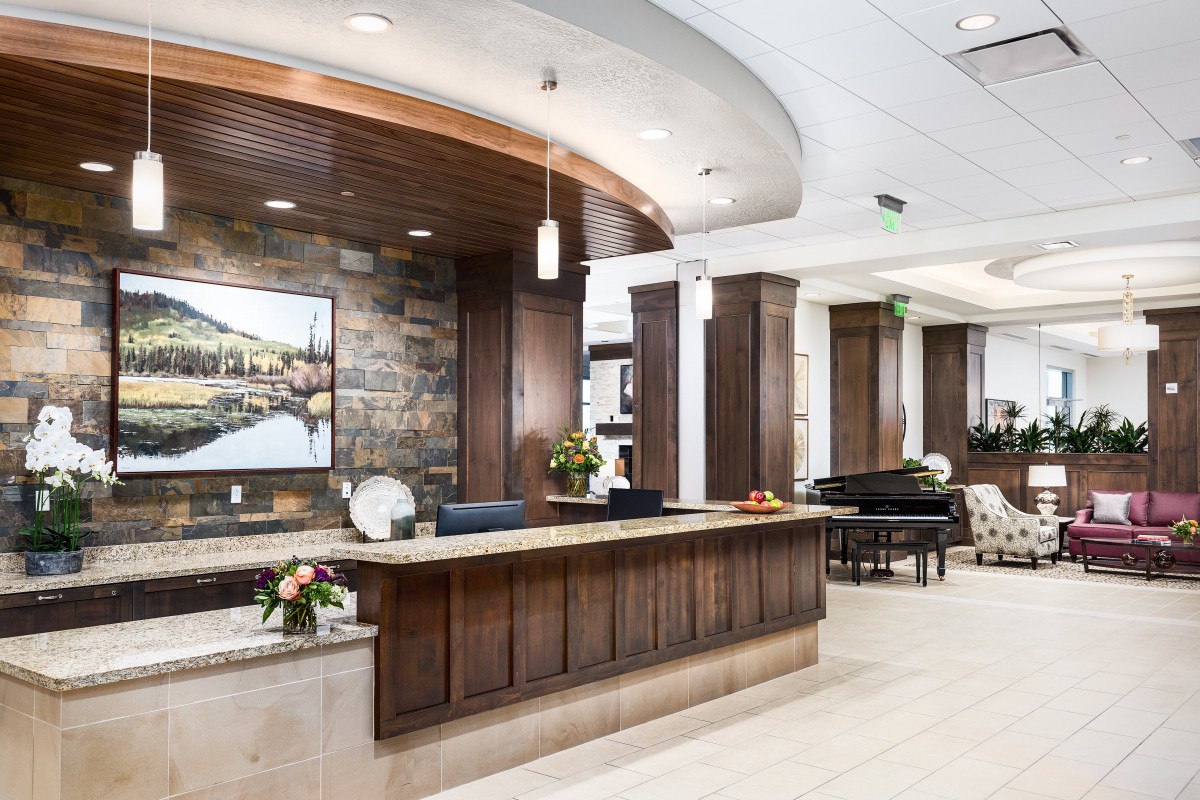 A modern lobby with a wooden reception desk, decorative flowers, and a grand piano.