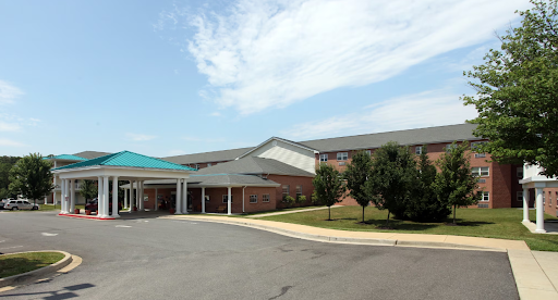 A modern healthcare facility viewed from the entrance, featuring a blue awning and landscaped surroundings.
