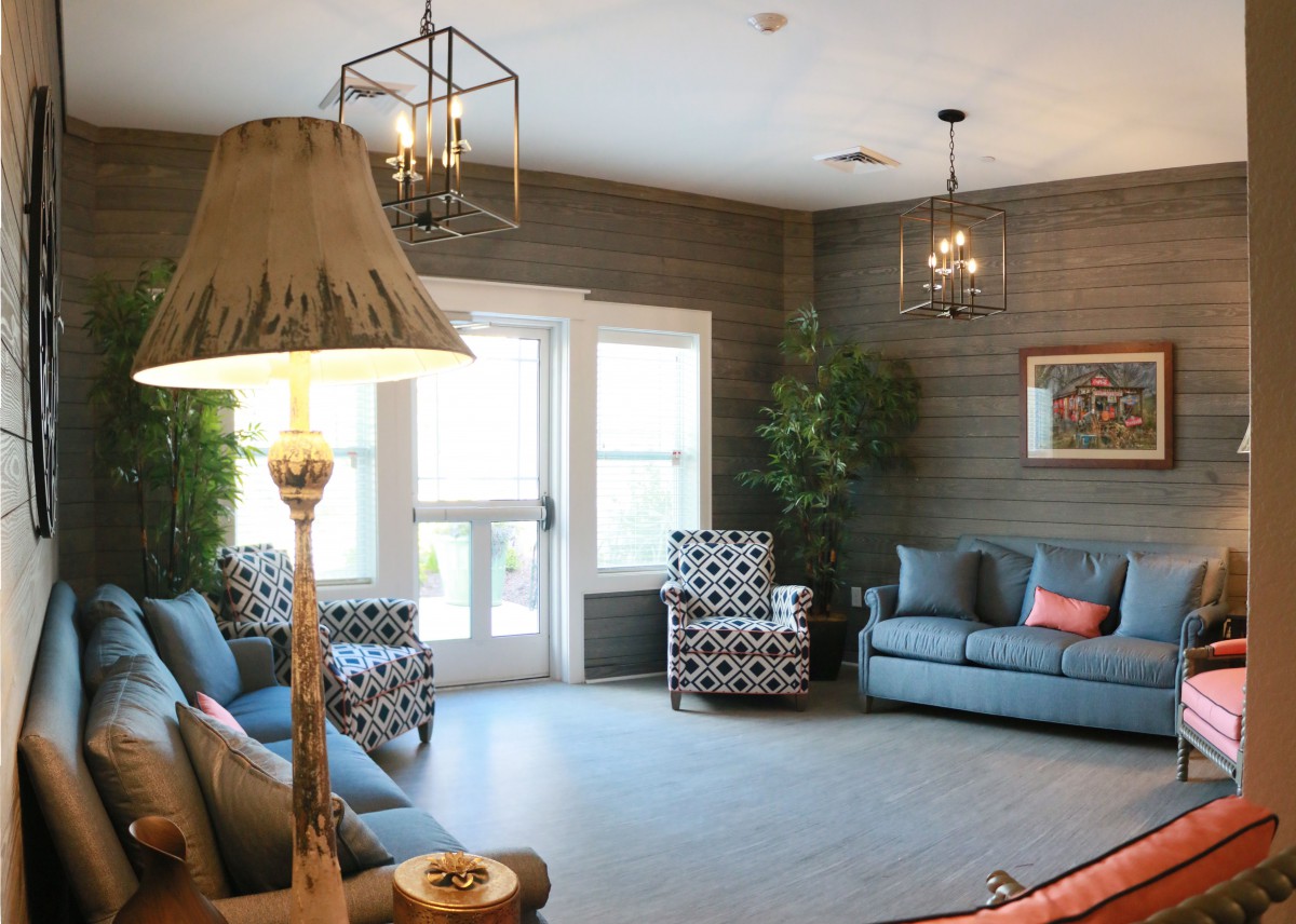 A cozy living room with modern decor, featuring a sofa, patterned armchairs, and large windows.