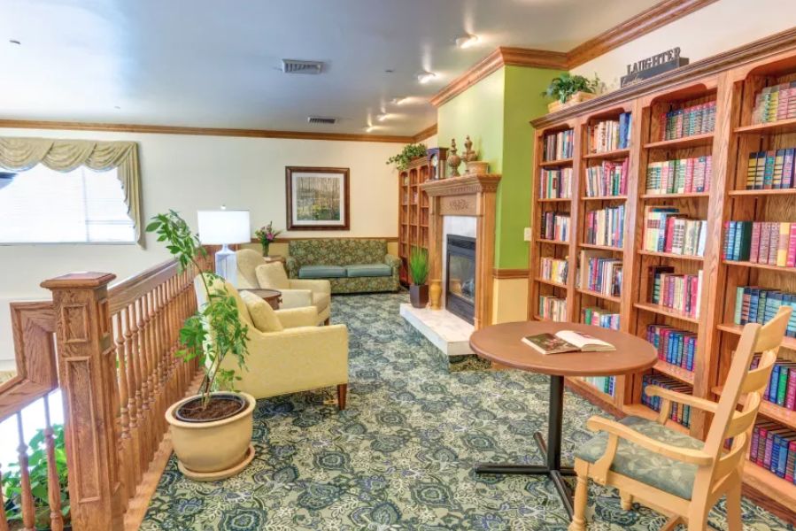 A cozy library space with bookshelves, armchairs, and a fireplace.