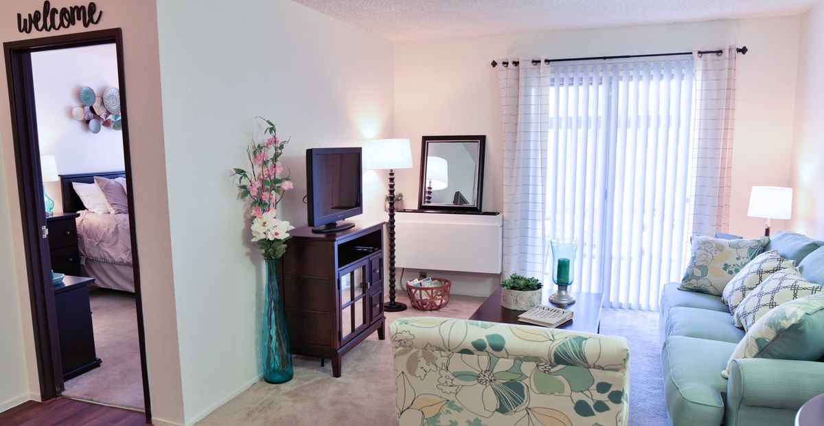 A cozy living room with modern decor, featuring a TV stand, lamp, and a patterned sofa.