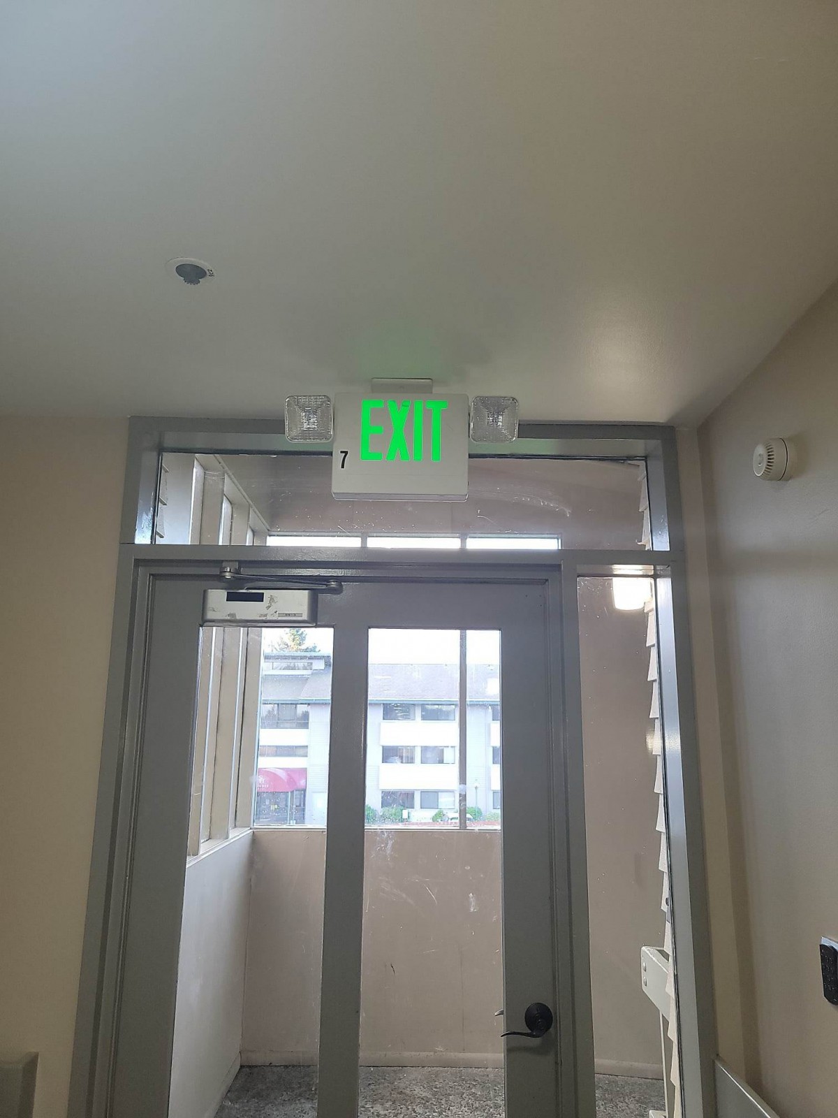 A building interior with an illuminated green exit sign above a glass door.