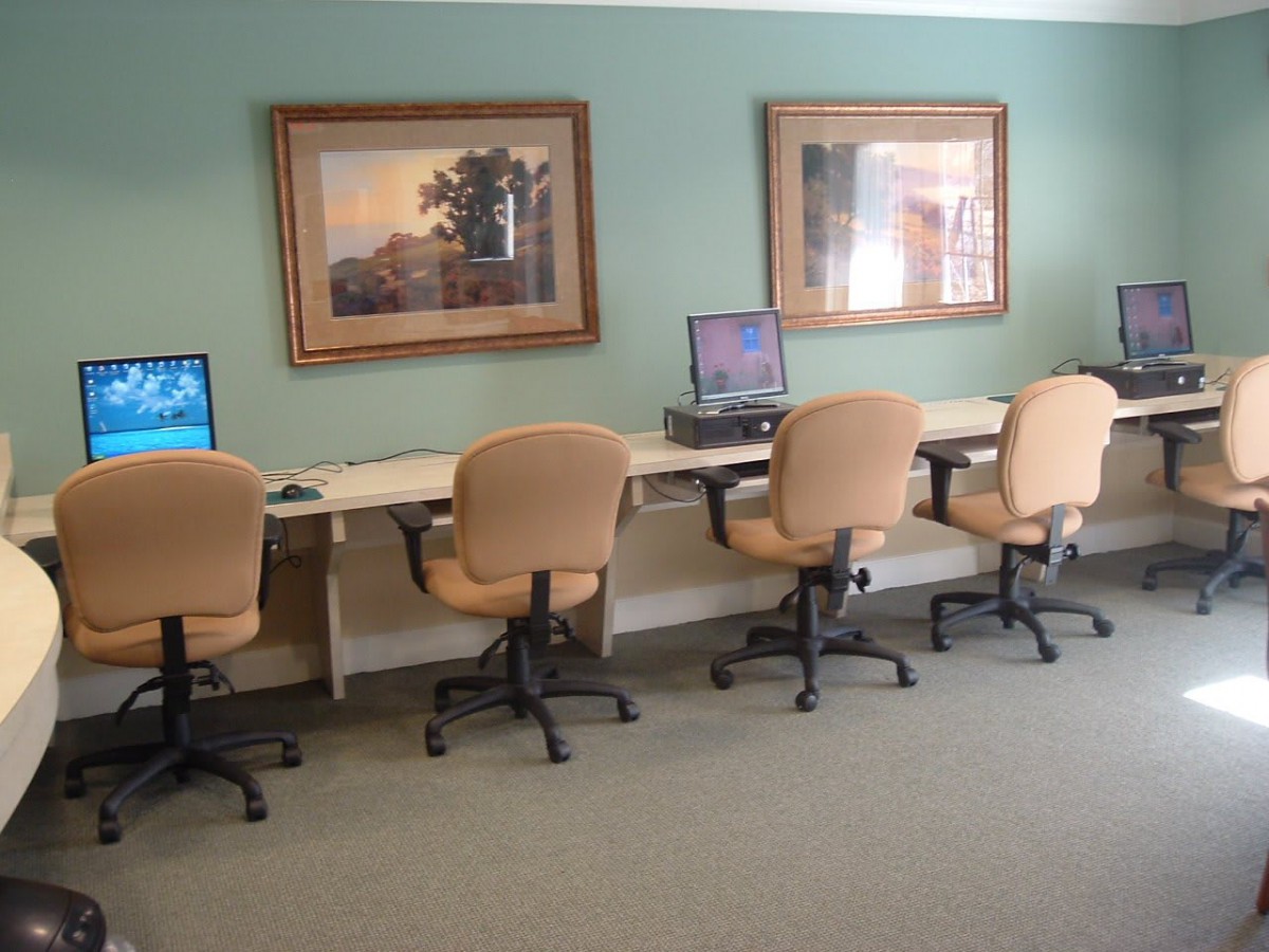 A computer lab with workstations and chairs lined against the wall, featuring framed paintings above.
