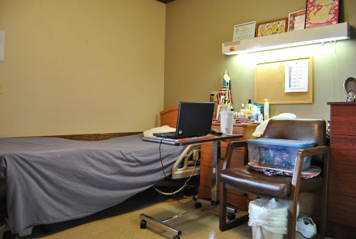 A view of a patient room in a hospital, featuring a bed, desk with a laptop, and various medical supplies.