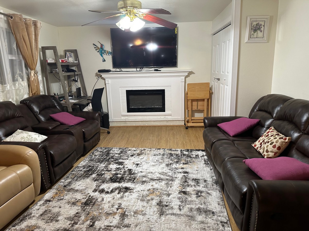 A cozy living room with two leather sofas, a fireplace, and a large TV mounted above it.