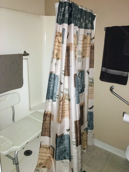 A bathroom featuring a patterned shower curtain and towels hanging on the wall.
