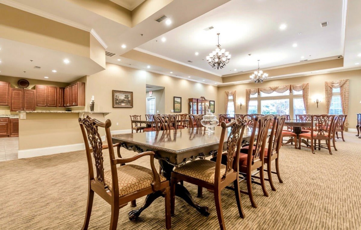 Elegant dining room with a large table and ornate chairs, illuminated by chandeliers.