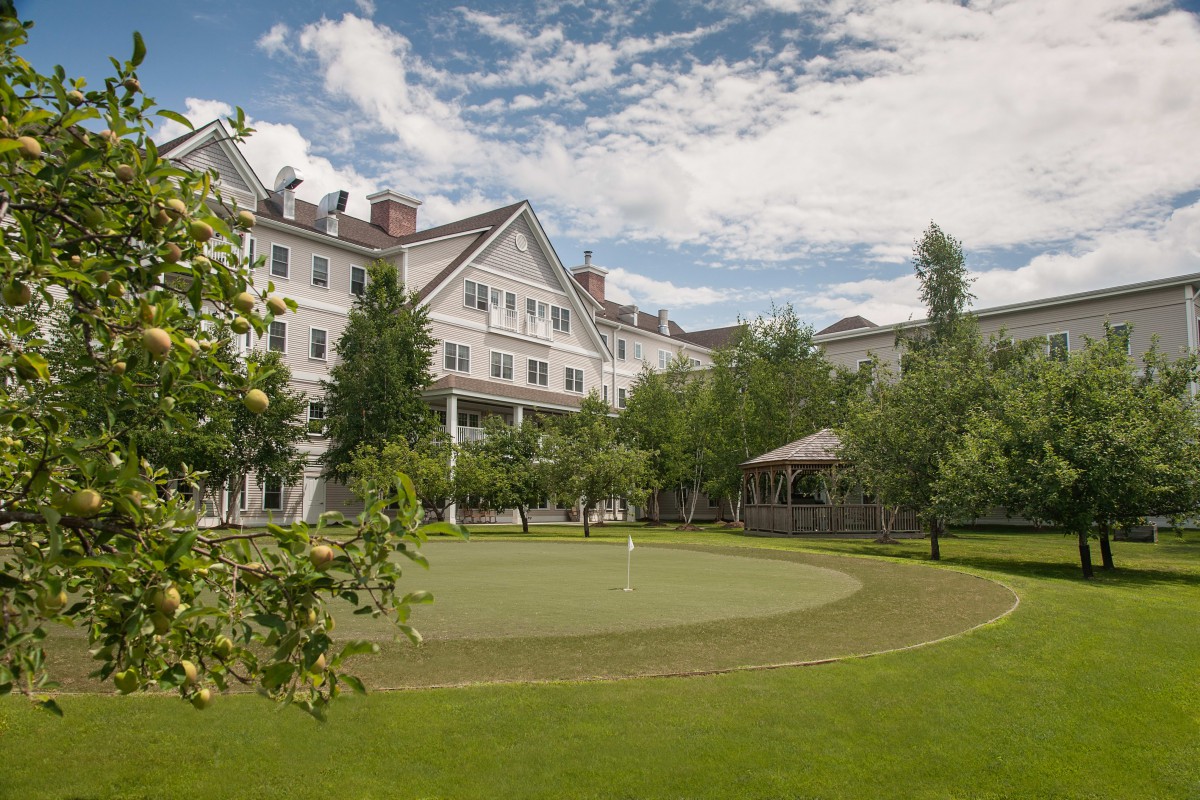 A grand hotel surrounded by lush greenery and a well-maintained lawn under a partly cloudy sky.