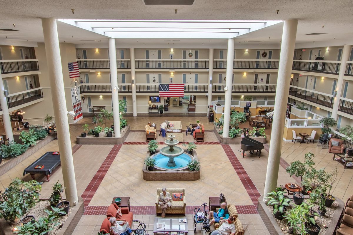 A spacious hotel atrium featuring a central fountain, seating areas, and lush greenery under ample natural lighting.