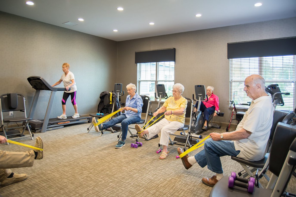A group of seniors participating in a fitness session using resistance bands and a treadmill in an indoor setting.