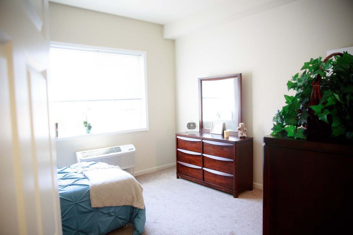 A bright and minimalist bedroom with a bed, dresser, and mirror.