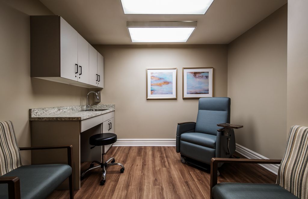 A clean and modern examination room with a comfortable chair, desk, and medical equipment.