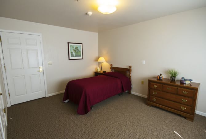 A minimalist bedroom with a single bed, lamp, and dresser.