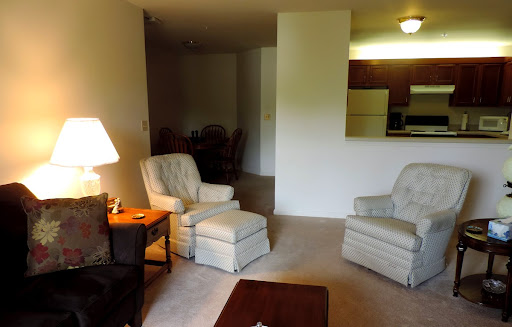 A cozy living room featuring two armchairs, a side table with a lamp, and an open view to the kitchen area.