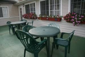 An outdoor patio area with green plastic chairs and tables, adorned with flower boxes on the windowsills.