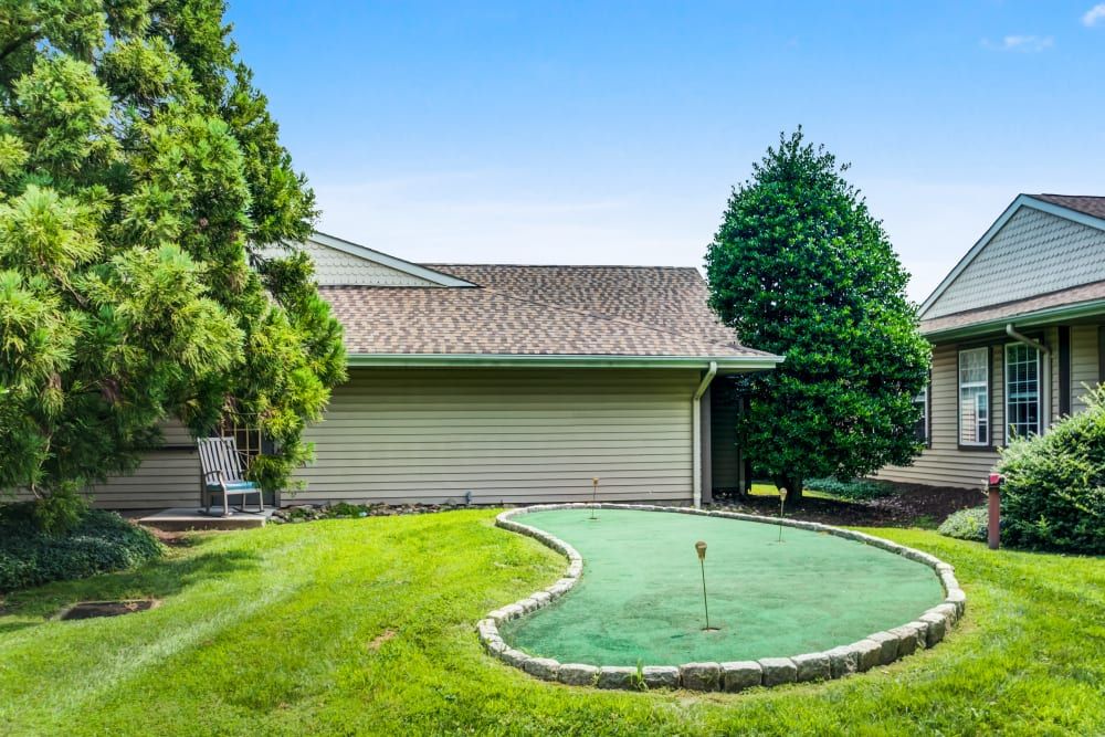 A cozy backyard featuring a putting green surrounded by lush grass and trees.