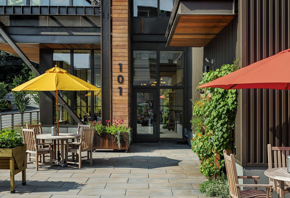 Outdoor patio area with colorful umbrellas and planters outside a modern building entrance.