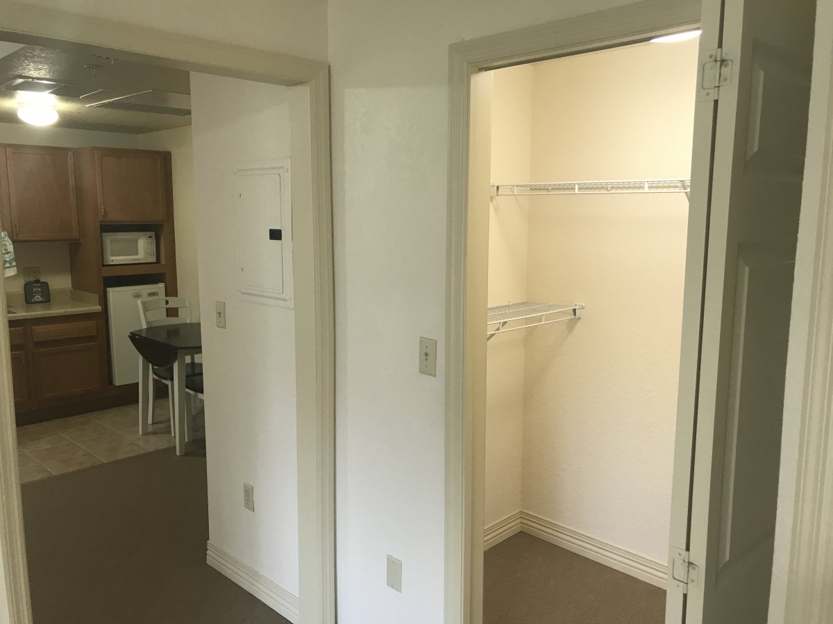 An interior view of an apartment showing a hallway with a closet and part of the kitchen.