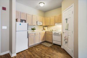 A small, cozy kitchen with light wood cabinets, a refrigerator, stove, and microwave.