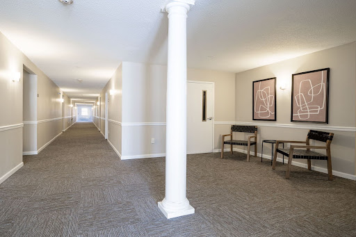 A well-lit interior hallway featuring a column, carpeted floor, and artwork on the walls.