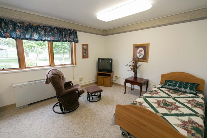 A cozy bedroom with a wooden bed, a TV on a stand, a comfortable chair, and decorative elements.