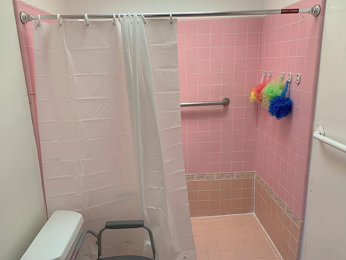 A bathroom with pink tiles, a shower curtain, and colorful loofahs hanging from a towel rack.