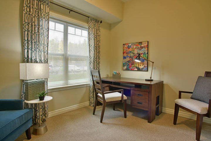 A cozy home office with a desk by the window, featuring a lamp and artwork on the wall.