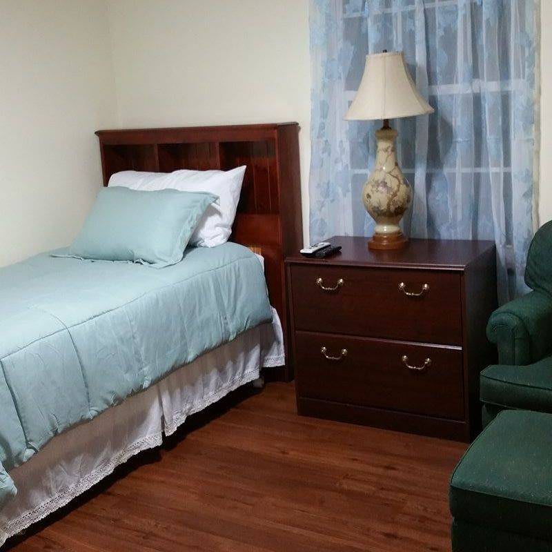 A cozy bedroom with a single bed, nightstand, and armchair.