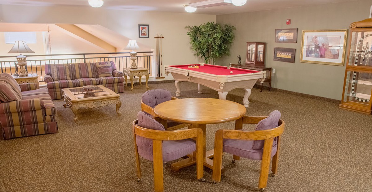 A cozy game room featuring a red-felt pool table, comfortable seating, and stylish decor.
