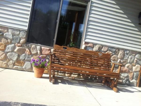 A wicker bench on a patio next to a planter with flowers, set against a stone wall.
