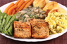 A plate featuring a balanced meal with tofu, carrots, green beans, gravy, scrambled eggs, and cornbread.