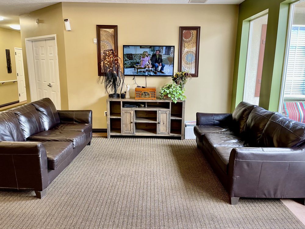 A cozy living room with two leather sofas facing a TV and cabinet, enhanced by decorative plants and wall art.