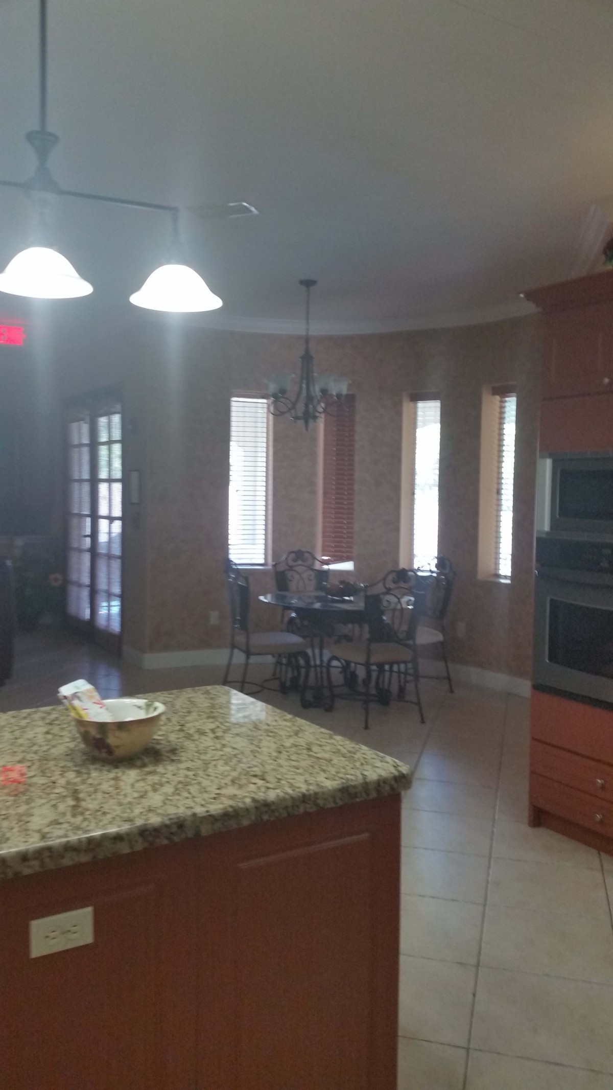A kitchen with a granite countertop adjacent to a dining area with windows and a table.