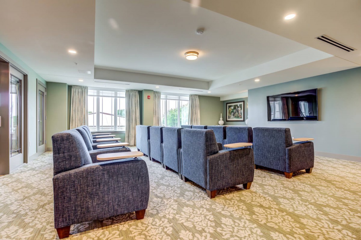 A modern lounge area with comfortable seating and a large television, featuring ample natural light from the large windows.